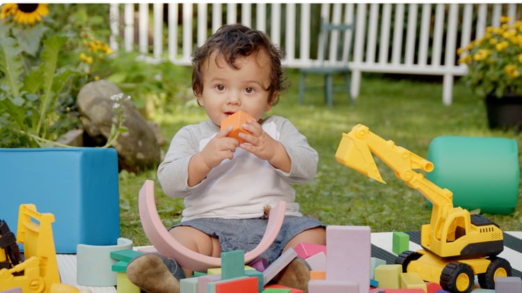 Toddler from Baby Baby playing outside with colorful blocks and toy excavators during a calm, imaginative play session.