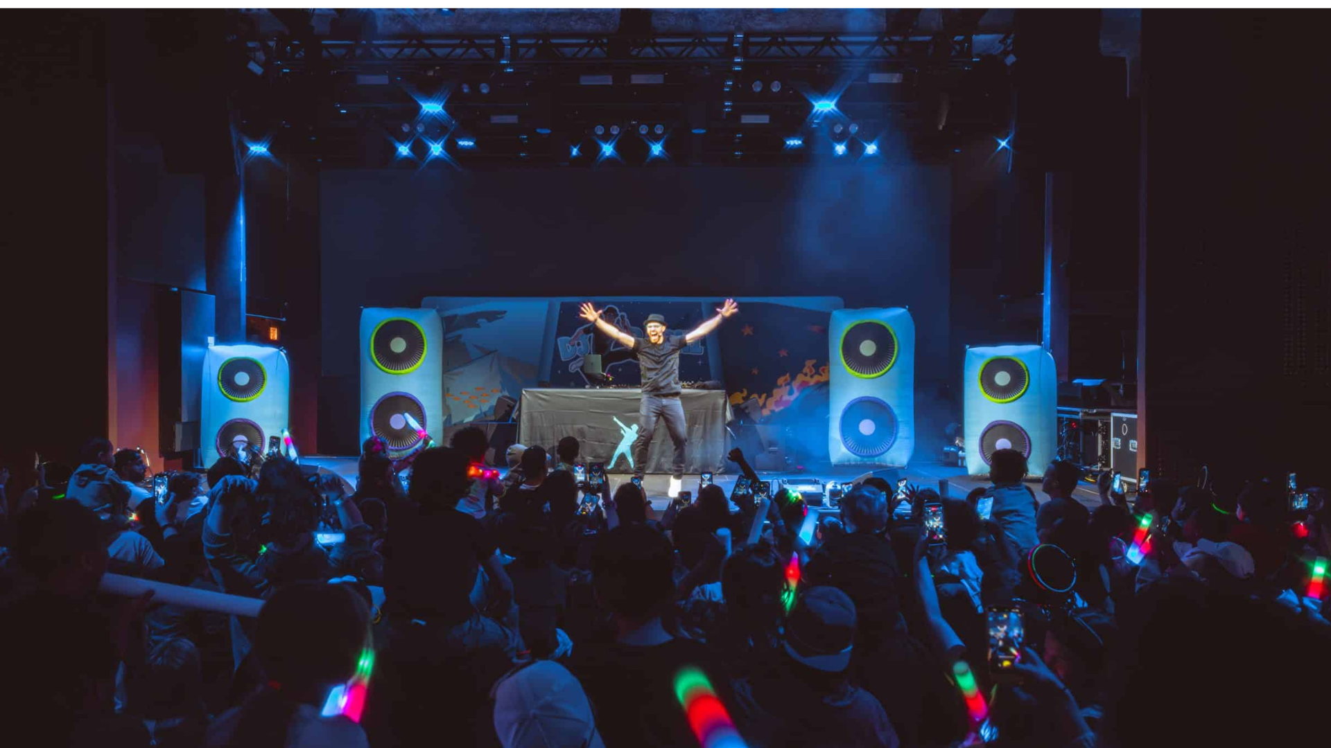 DJ Raphi performing on stage with arms raised at a Hype Tour concert, surrounded by glowing lights as kids and families dance in the crowd