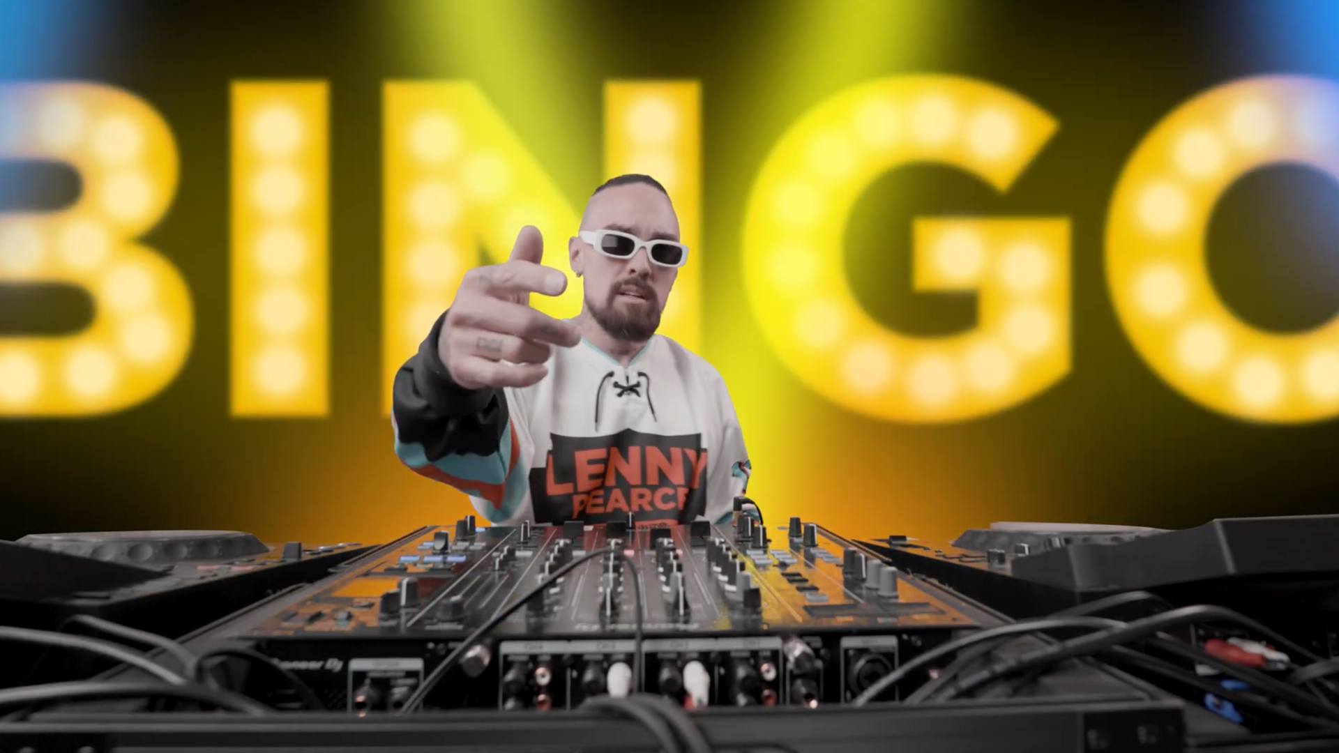 Lenny Pearce at a DJ mixer pointing at the camera in front of a glowing yellow BINGO sign, from his techno remix of the classic song